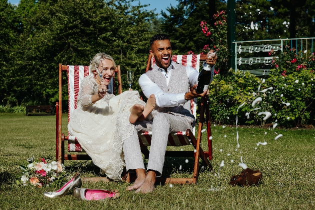 couple celebrataing their wedding by popping champagne sittin in deck chairs