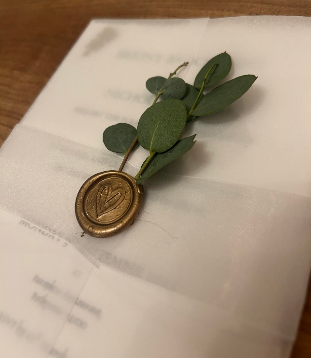 wedding invitation with greenery held by a gold wax seal by Topikki Stationery